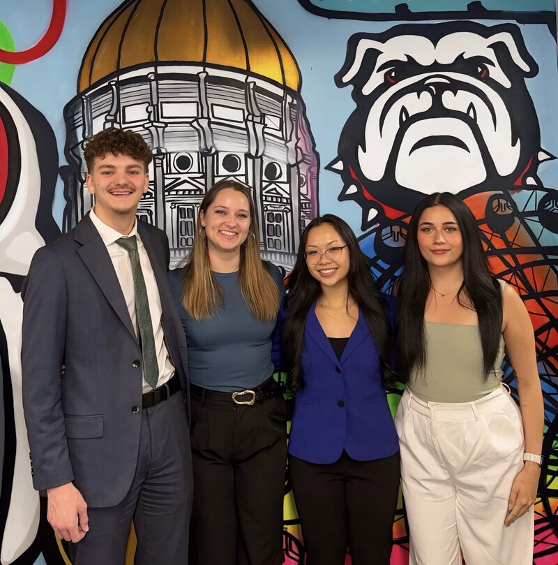 Four New Acquisitions team members in business attire standing together in front of an Atlanta mural in the office